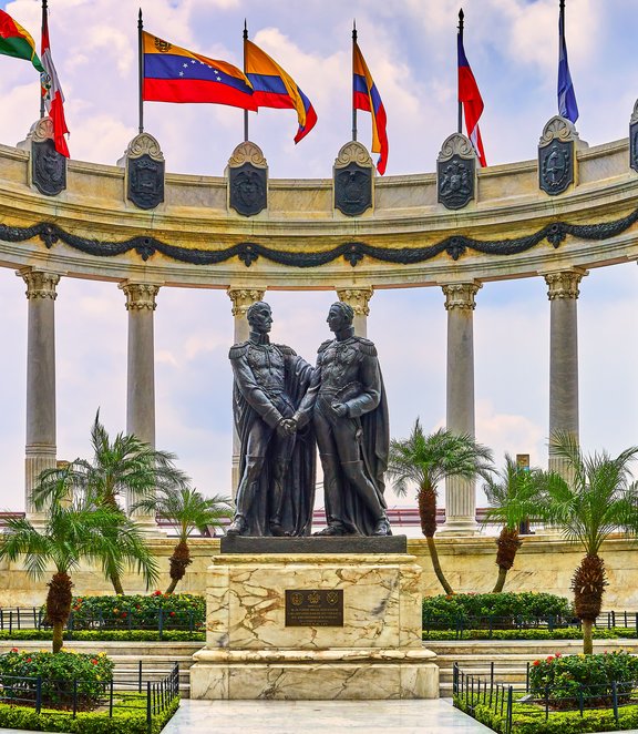 Monument to the Independence Heroes in Guayaquil, Ecuador, featuring statues of Simón Bolívar and José de San Martín surrounded by flags of Latin American countries and classical columns under a bright sky.