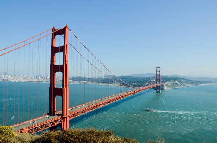 The Golden Gate Bridge in San Francisco stretching over the blue waters of the bay, with a boat passing underneath and the city visible in the background.