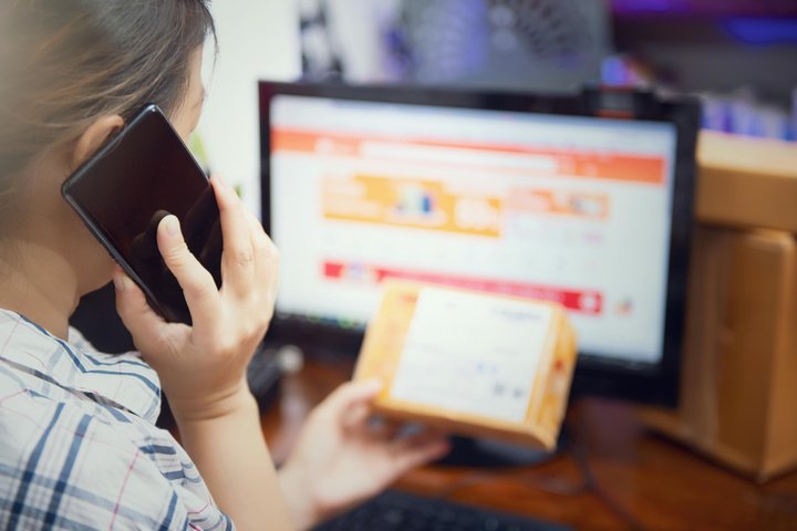 Person holding a parcel and speaking on the phone while shopping online, illustrating the growing number of people buying products through e-commerce.